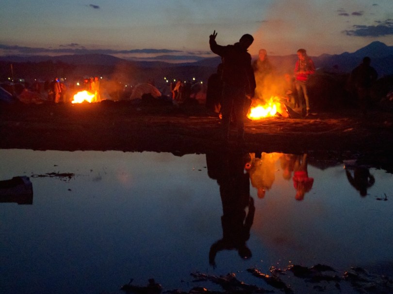A teenager plays with the camera in the reflections of a stagnant water pond next to their encampment